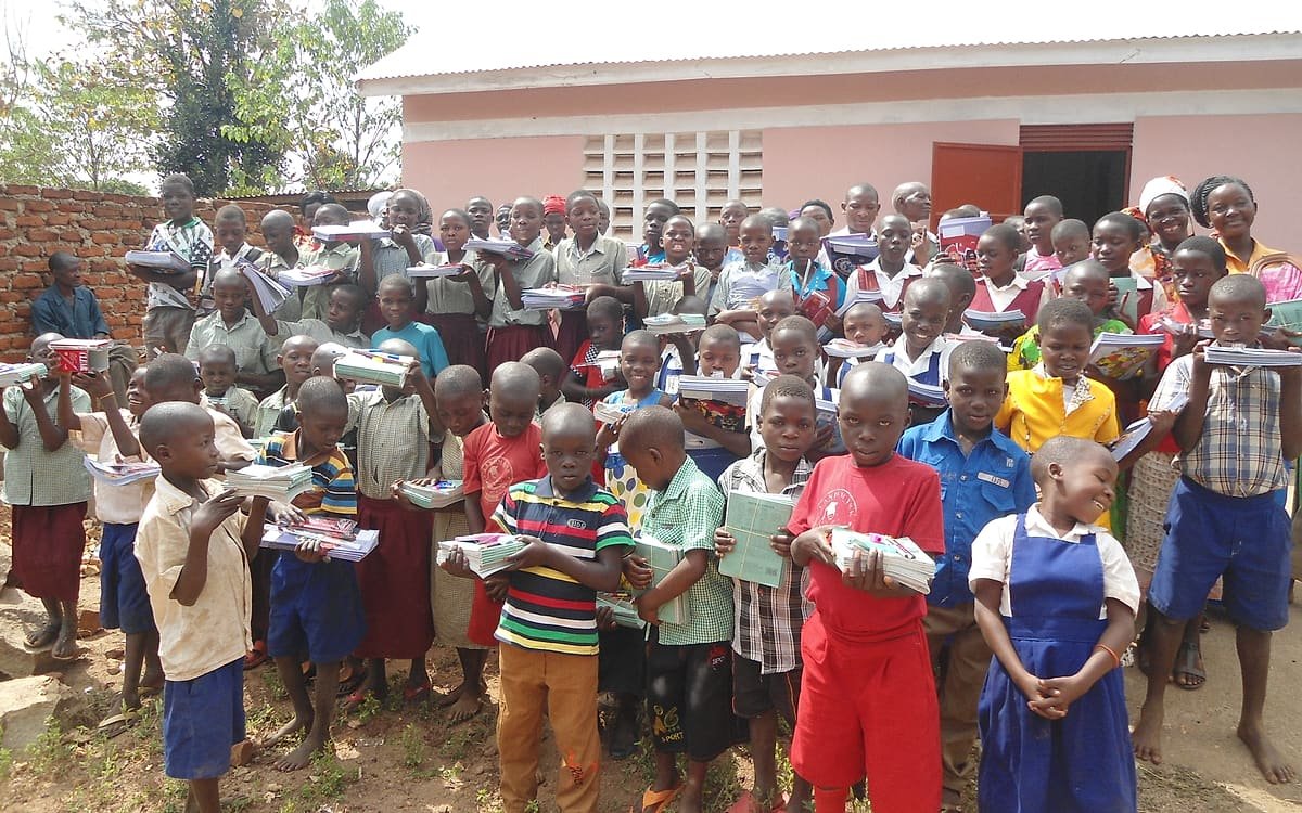 Pupils outside their school in Jinja District holding exercise books and scholastic materials received through a Kiyunga Social Service Centre school support activity.