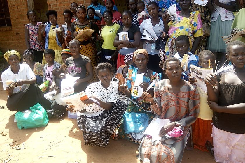 Women and girls holding hygiene and sanitary materials received at a Kiyunga Social Service Centre menstrual health activity.