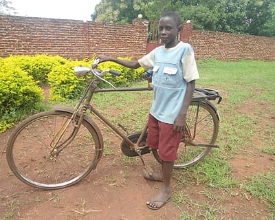 A boy standing beside a bicycle outside a village home.